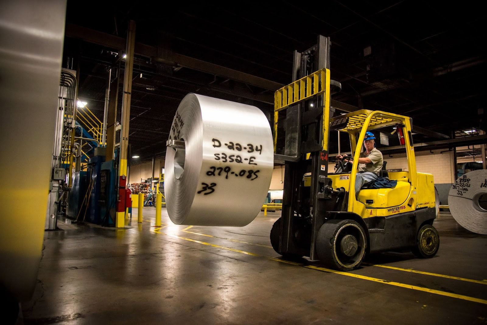 Forklift operator transporting a large aluminum coil through a warehouse at an Golden Aluminum mill.