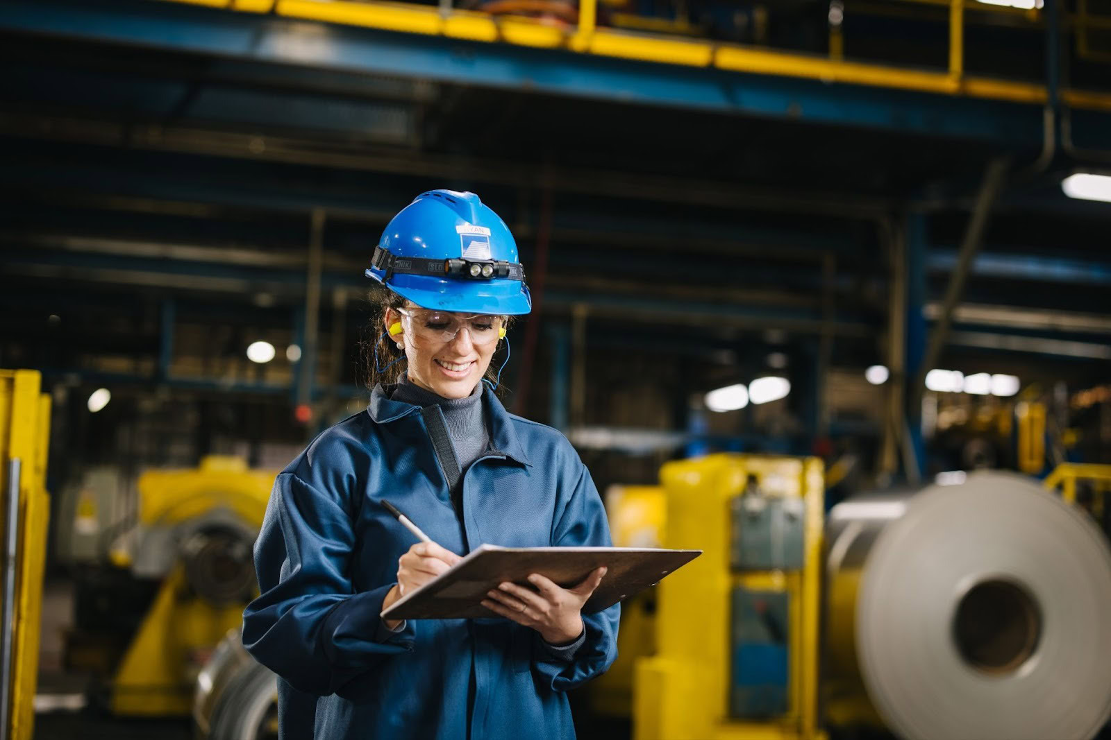 Quality team member reviewing data on a tablet near Golden Aluminum coils inside a rolling mill.