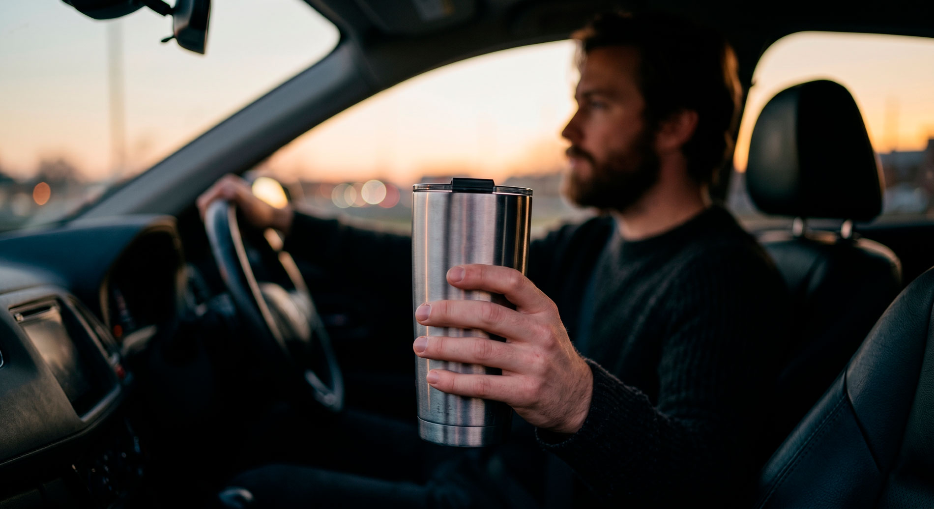 Man holding a stainless steel vacuum-insulated tumbler while driving, illustrating the everyday carry culture around insulated drinkware