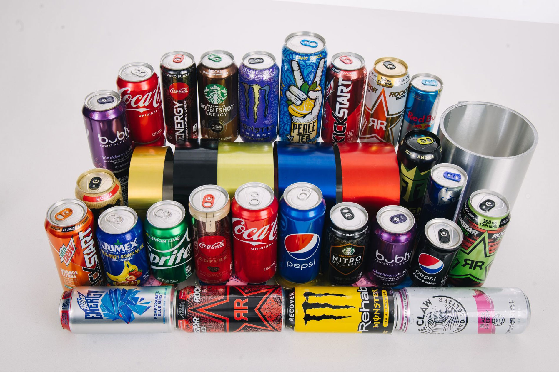 Collection of branded aluminum beverage cans in various colors and designs alongside a plain aluminum cylinder, representing the range of products that begin as flat-rolled aluminum sheet