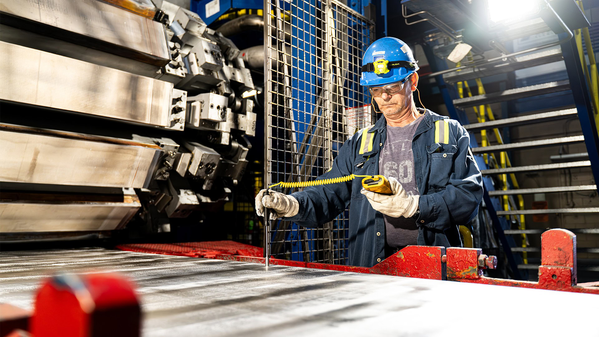 Worker holds a handheld gauge to aluminum strip to check thickness during cold rolling at Golden Aluminum.